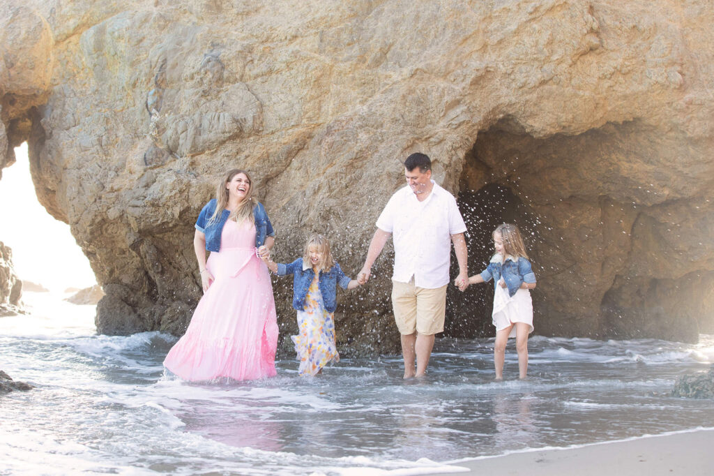 mom and dad with their two daughters dancing in the ocean at El Matador Beach in Malibu
