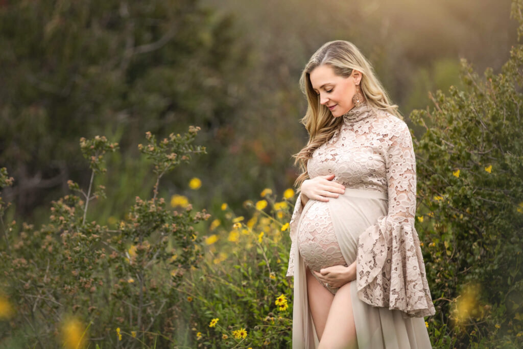 Mom to be at a maternity photoshoot, looking down at her bump in a beige maternity dress - Los Angeles Pediatricians