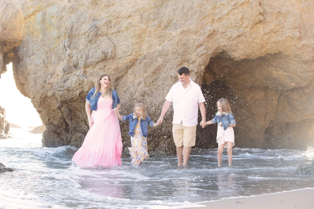 Family kicking the water and laughing at the beach in Malibu - beach photoshoot outfit ideas