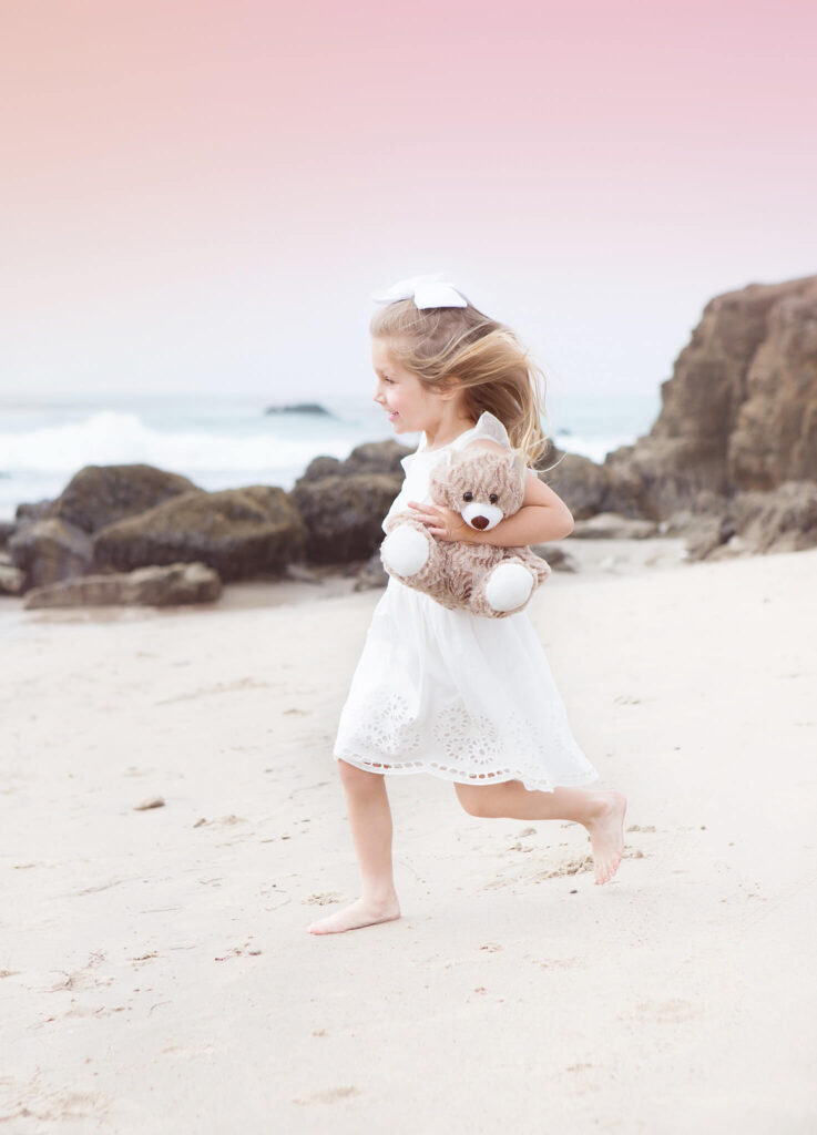 Little girl running along the sand with her teddy at the beach in Los Angeles