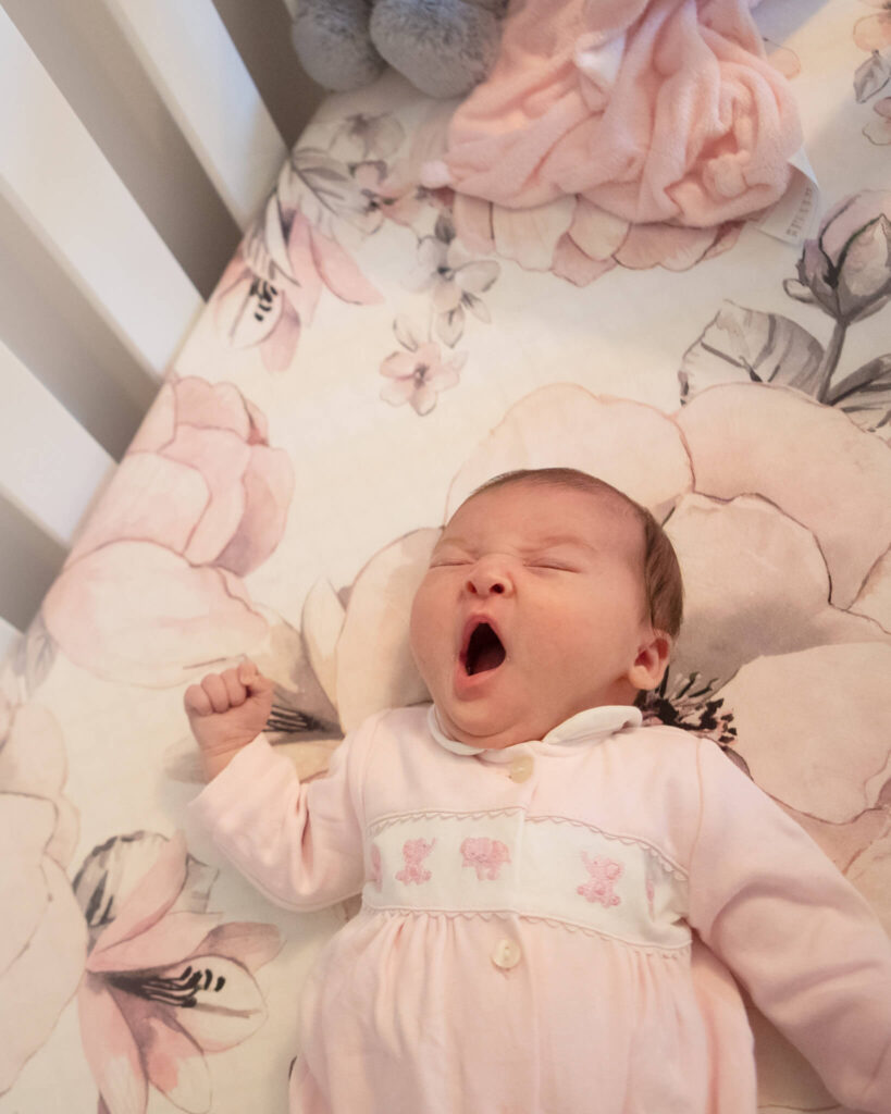 newborn baby yawning in her crib wearing a beautiful pink sleepsuit