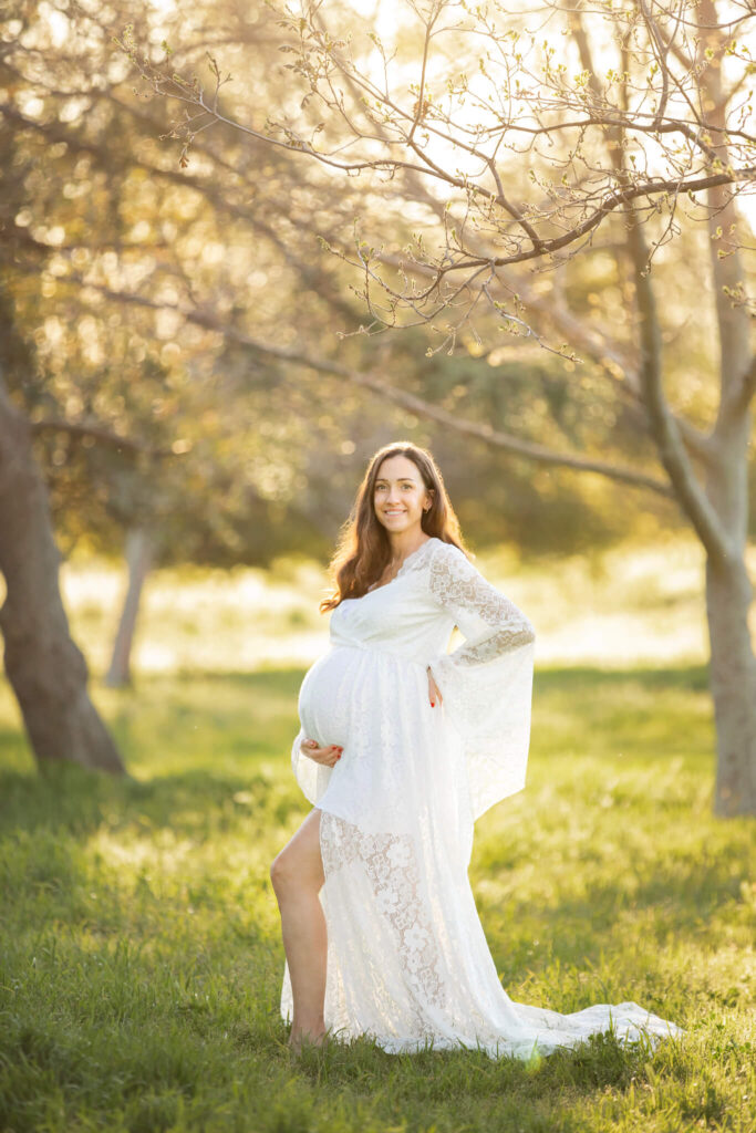Pregnant mom glowing in a white lace dress with the sunset glow behind her - Hatch Brentwood
