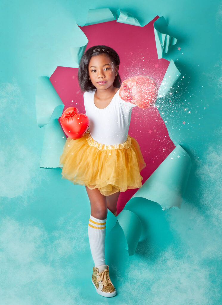 Little girl wearing boxing gloves punching through backdrop in photoshoot with Elsie Rose Photography - Indoor Playgrounds Los Angeles