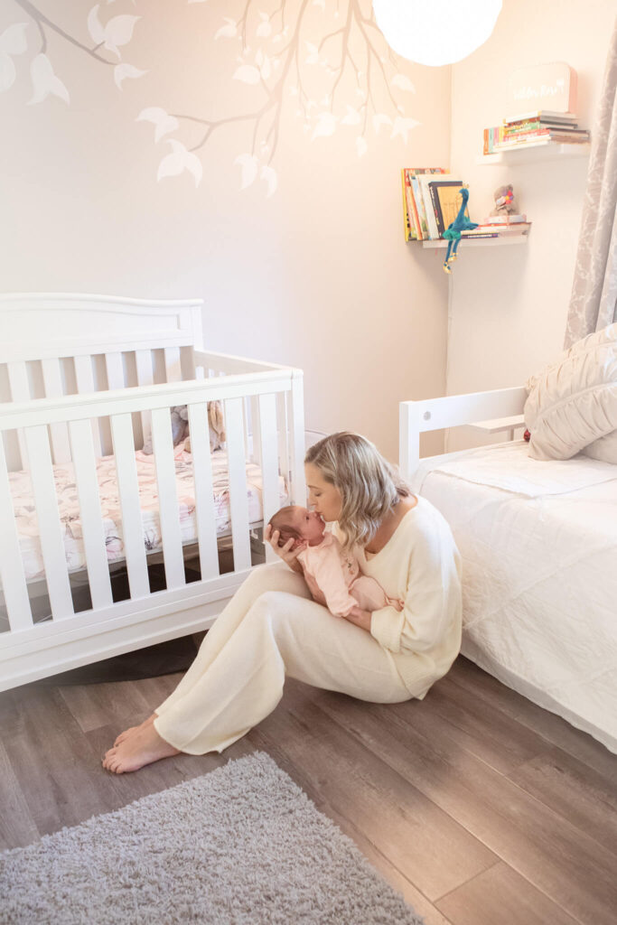 New mommy kissing her newborn daughter in her nursery, image all white with soft greys
