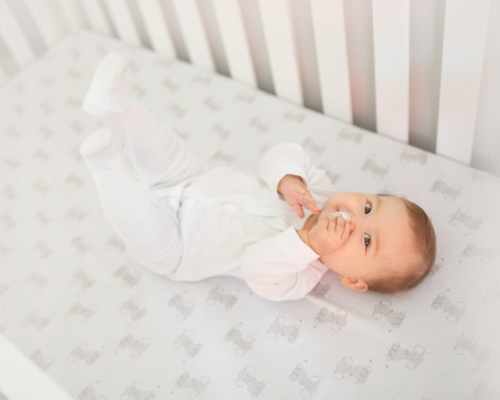 Baby laying on her back in crib with feet up in the air with image taken in a lifestyle vibe - Los Angeles Lactation Consultant