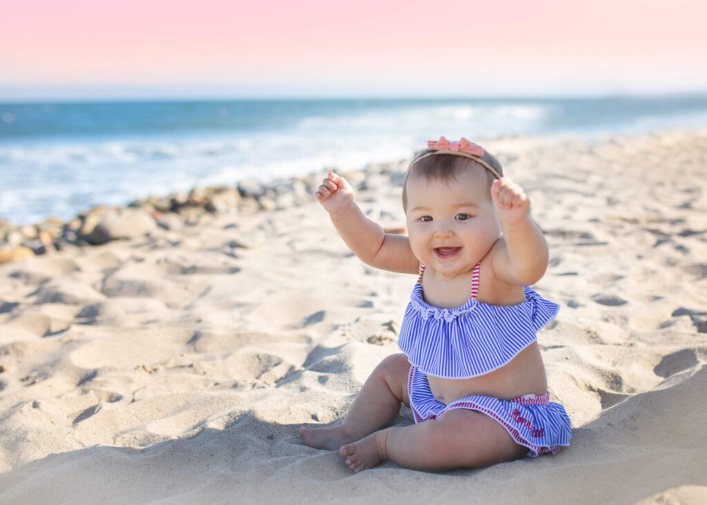 Baby girl in Monnalisa Beverly Hills swimsuit at the beach in Malibu lifting up the sand