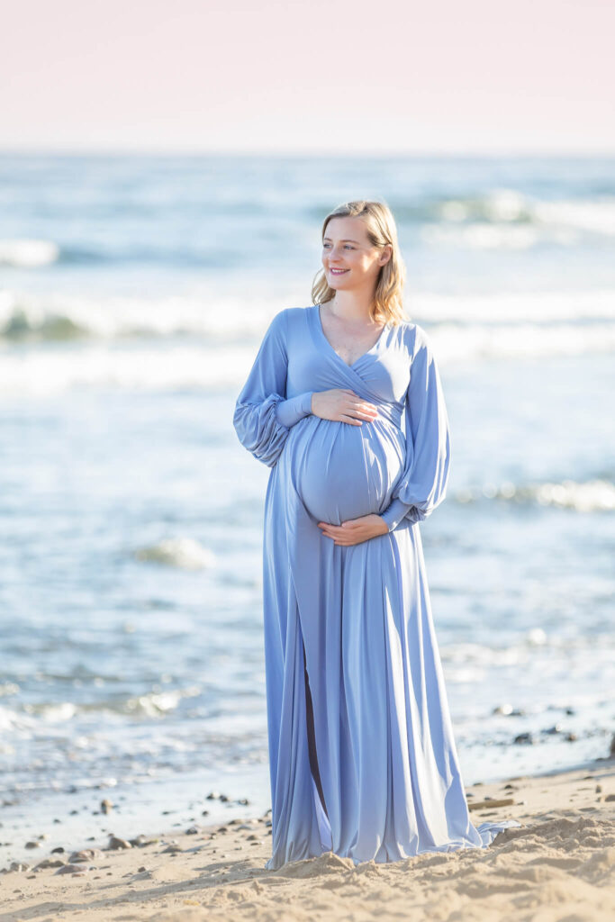 Mom to be holding her baby bump in a maternity photoshoot in Malibu with pink sky behind