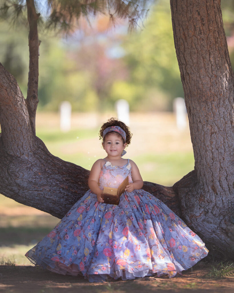 Little girl in a tree in a blue and flowers dress like a princess photographed by Woodland Hills photographer - Couture Kids on Robertson