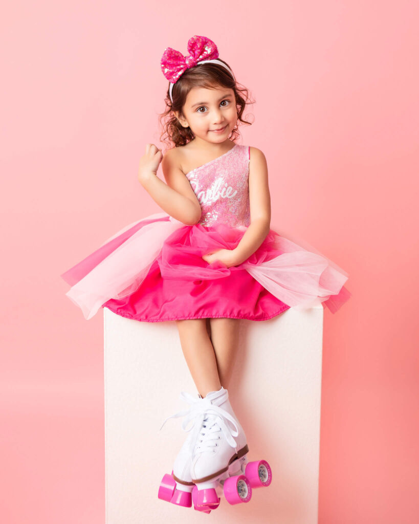 Little girl sitting on a box wearing rollerskates with a pink barbie dress photographed in LA - pediatric dentist los angeles