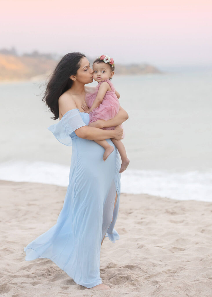 Mom wearing a blue dress with her baby daughter wearing a pink dress at the beach in Malibu - santa monica beach hotels