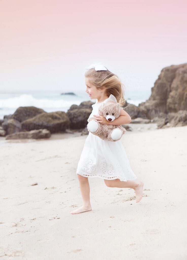 Little girl in white running along the beach front holding her teddy - santa monica beach hotels