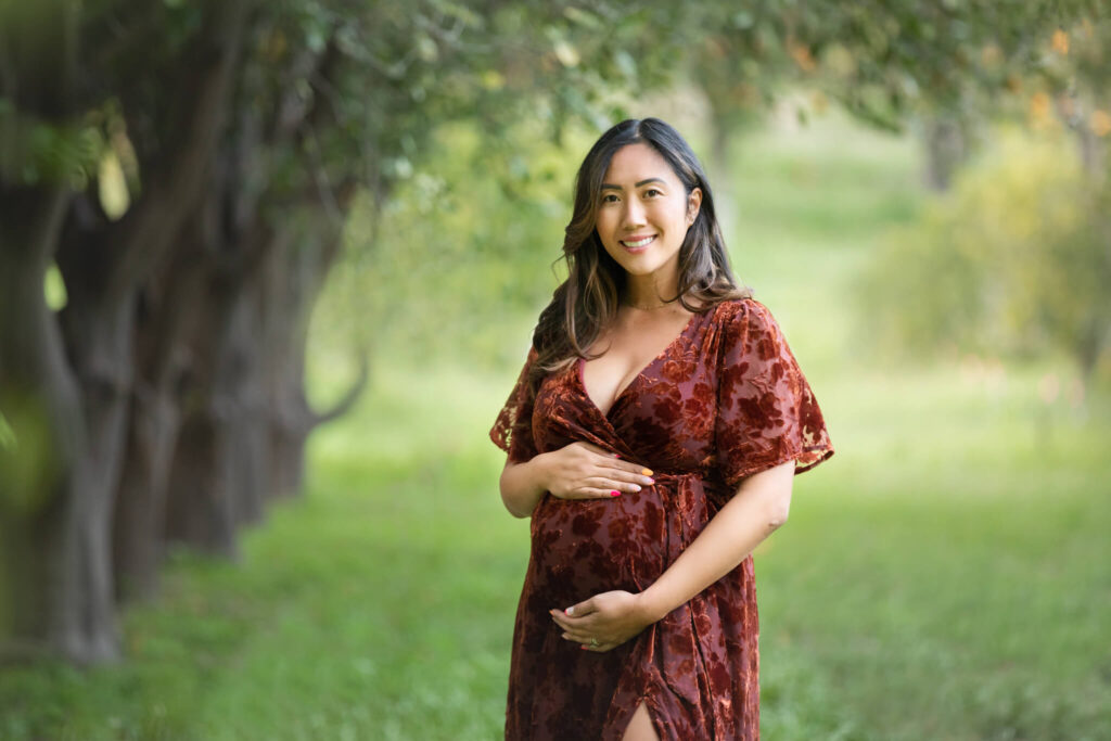 Image of mother to be in an orange dress smiling and holding baby bump taken by LA photographer Elsie Rose Photography