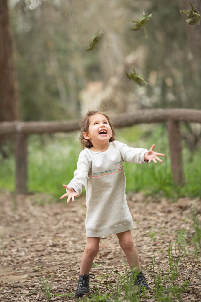 Little girl in cream dress throwing leaves and laughing in the park