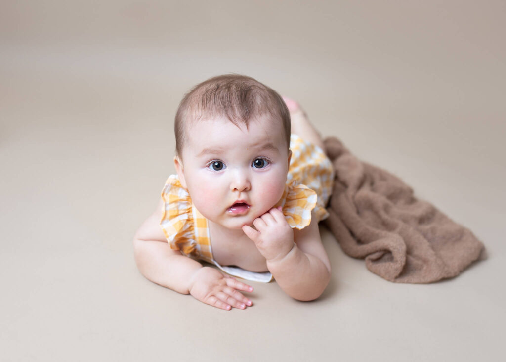 Baby girl leaning on hand in yellow romper by LA photographer