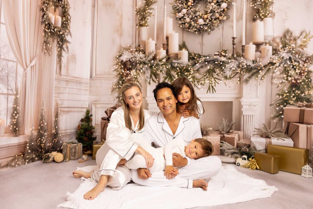 Family in white Christmas pjamas smiling to the camera and sitting on the floor