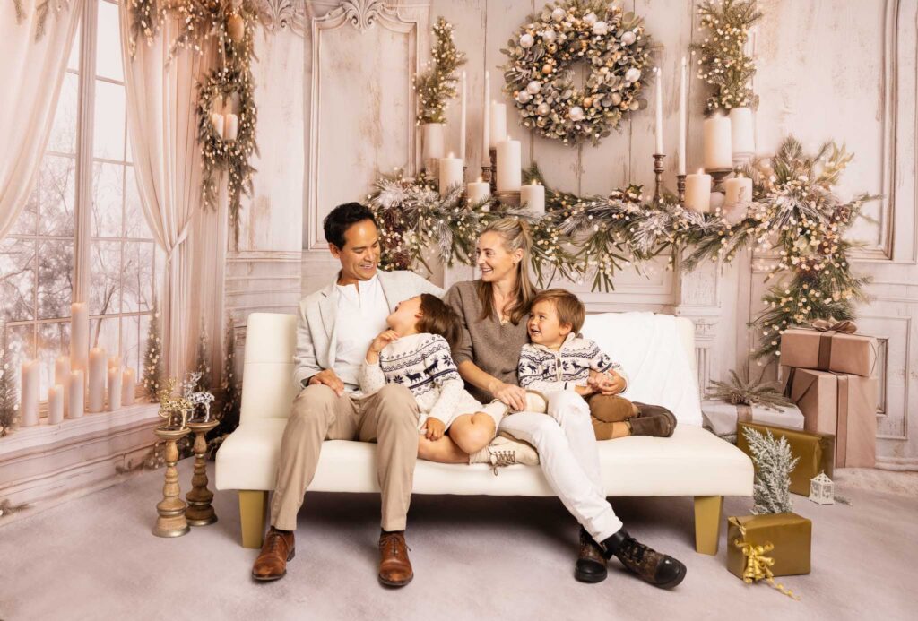Mom, dad and two children sitting on a white sofa for a photoshoot at Christmas time in Los Angeles